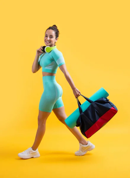 glad fitness woman in sportswear walk with sport bag in studio. fitness woman in workout sportswear isolated on yellow background. fitness and sportswear.