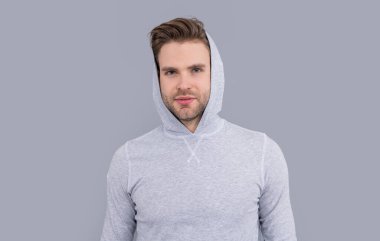Erkek portresi. Yakışıklı adam sıradan bir kapüşonlu giyiyor. Tıraşsız yüzlü genç bir adam. Beyazların stüdyosu gri arka planda izole edilmiş..