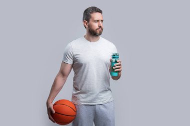 Sporcu basketbolcu, gri arka planda izole edilmiş su içiyor. Stüdyoda sporcu basketbolcu. Basketbolcu bir sporcunun fotoğrafı. Spor giyim sektöründe basketbolcu.