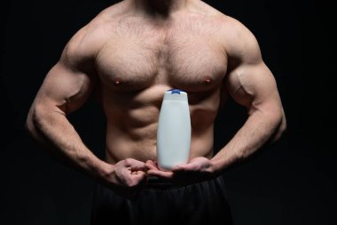 Erkek kozmetik ürünleri olan kaslı adam siyah arka planda izole edilmiş. Stüdyoda kozmetik ürünleri satan kaslı bir adam. Güçlü kaslı adam kozmetik ürünlerini elinde tutuyor. Erkek makyaj şampuanıyla kaslı bir adamın fotoğrafı..