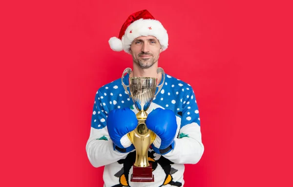 christmas man with champion cup celebrating victory in studio. man celebrating chirstmas victory isolated on red background. christmas victory celebration.