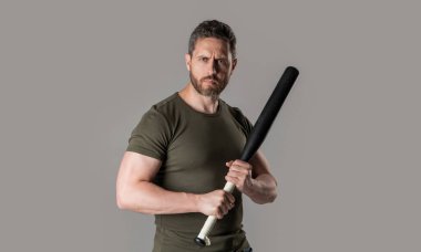 Stüdyoda beyzbol sopası olan kaslı bir suçlu. Sopalı suçlu adamın fotoğrafı. Yarasayla tehdit eden bir suçlu. Gri arka planda yarasalı bir suçlu var..