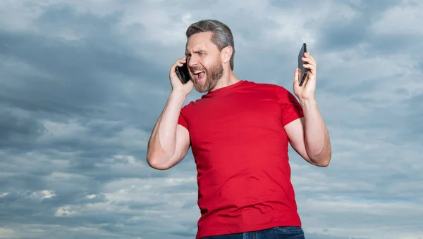 angry man has phone talk wear red tshirt. photo of man has phone talk. man has phone talk on sky background. man has phone talk outdoor.