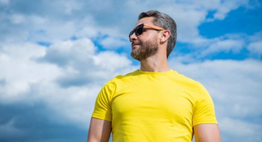 Gökyüzü arka planında sarı gömlekli ve güneş gözlüklü adam. Boşluğu kopyala.