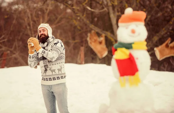 Snowman and cheerful bearded hipster knitted hat and warm gloves play with snow outdoors. Christmas holidays. Active lifestyle. Snow games. Leisure on fresh air. Have fun winter day. Let it snow.
