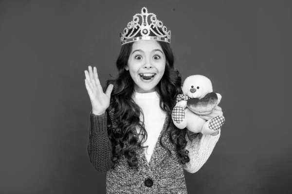 amazed happy child in queen crown. princess in tiara. kid hold bear toy. teen girl wear diadem on red background. happy childhood.