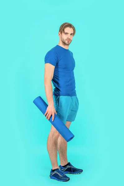 sport man with fitness yoga mat isolated on blue background. sport man with yoga mat in studio. photo of sport man with yoga mat. sport man with yoga mat wearing sportswear.