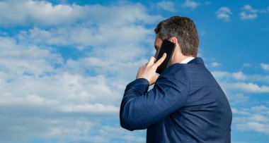 İnsanın arka plandaki görüntüsünde açık havada telefon konuşması, kopyalama alanı var. Adamın telefonda konuşma kıyafeti var. Adamın fotoğrafı telefonda konuşuluyor. Adamın gökyüzü geçmişinde telefon konuşması var..