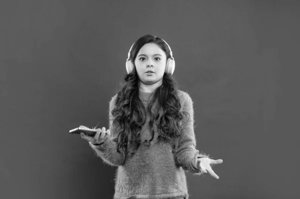 confused kid wear sweater. express emotion. autumn fashion. teen girl in earphones use smartphone. modern life in childhood. listening audio book. child listen music in headphones.