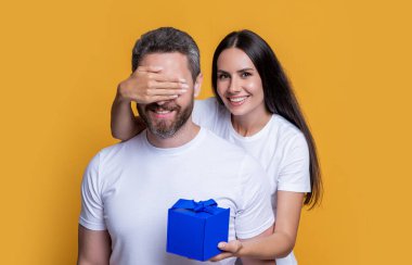 happy surprise couple with present in studio. holiday couple with present box. photo of couple with present for holiday surprise. mens day. couple with surprise present isolated on yellow background. clipart