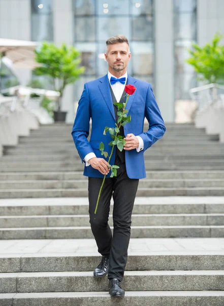 elegant man in tux. man wearing tux bowtie outdoor. handsome tux man with red rose.