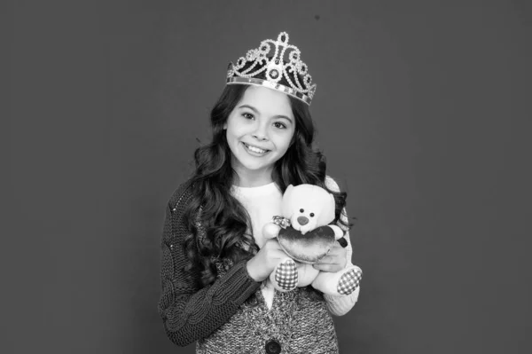 happy child in queen crown. princess in tiara. kid holding bear toy. teen girl wear diadem on red background. happy childhood.