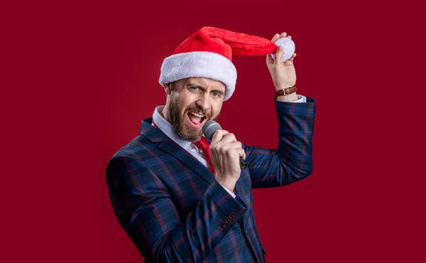xmas event host man singing. xmas event host man singing in santa hat. event host man singing with microphone. merry xmas. event host man singing at xmas isolated on red.