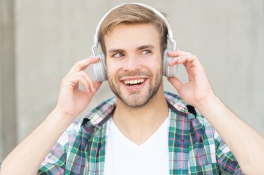 Dışarıda müzik dinleyen bir adam. Müzik dinleyen ve kareli gömlek giyen yakışıklı bir adam. Kulaklıkla müzik dinleyen bir adamın fotoğrafı. Adam açık havada müzik dinliyor..