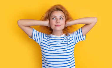 Neşeli kızıl kız sarı arka planda izole edilmiş gürültülü sesler duyuyor. Genç kız stüdyoda gürültülü sesler duyuyor. Ses kız için çok yüksek ve gürültülü.,