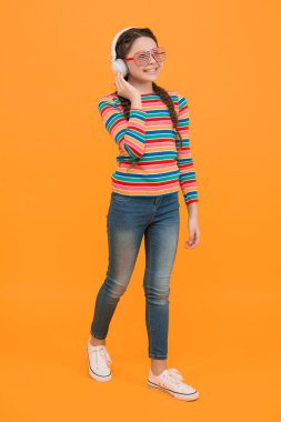 Saçları örgülü mutlu genç kız gökkuşağı rengi ve görkemli parti gözlükleri takıyor sarı arka planda kulaklıkla müzik dinliyor, müzik dinliyor..