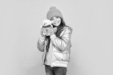 Kışlık elbiseli mutlu genç kız mavi arka planda oyuncak tutuyor, çocukluk..