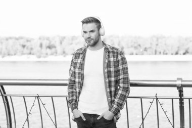 Dişli gömlekli, kulaklıklı, dışarıda müzik çalan sakallı bir genç..