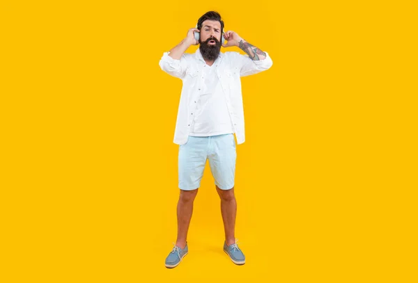 confused bearded man listening music in headphones isolated on yellow. man listening music in headphones. listen to music concept. studio shot of man with headphones. cool man listening music.