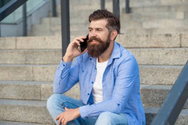 Neşeli adamın dışarıda akıllı telefonu var. Adamın sokakta akıllı telefonları var. Adamın fotoğrafında akıllı telefon var. Adamın açık havada akıllı telefonu var..