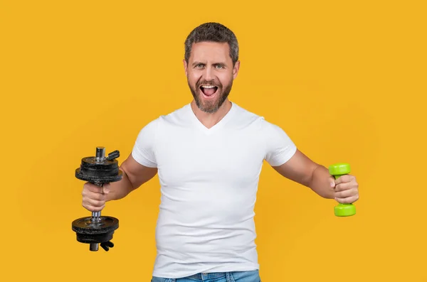shouting strong sport man training with dumbbell. strong sport man training with dumbbell isolated on yellow. strong sport man training with dumbbell in studio. strong sport man training with dumbbell
