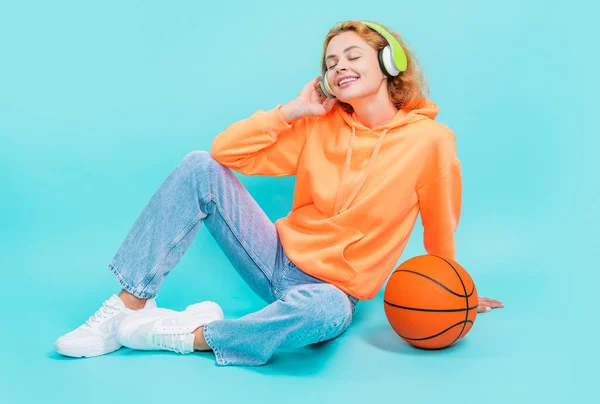 glad redhead basketball woman player on color background. basketball woman player isolated on blue background. basketball woman player at studio. photo of basketball woman player in hoodie.