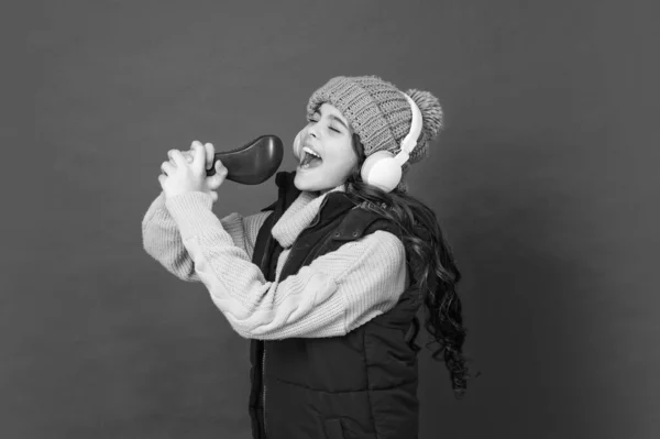 teen girl in hat and earphones singing in comb. modern life in childhood. karaoke. happy child listen music in headphones. kid wear warm clothes. express positive emotion. winter fashion.