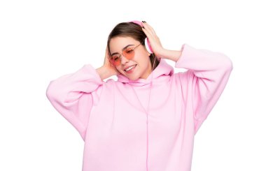 Pembe kapüşonlu ve gözlüklü mutlu genç kadın beyaz kulaklıklarla müzik dinlemenin keyfini çıkarıyor..