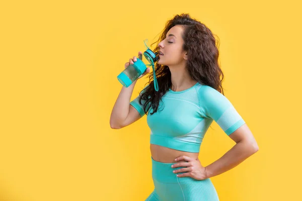 fitness woman drinking sport water bottle in studio. fitness woman drinking sport water bottle isolated on yellow background. fitness and sport.