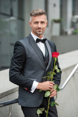 Siyah smokinli zarif adam. Smokin giymiş, papyonlu bir adam. Kırmızı güllü neşeli smokinli adam..