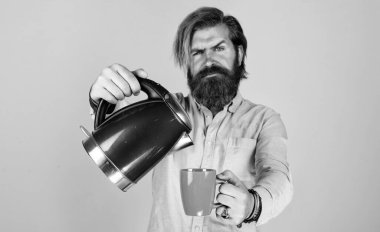 Biraz daha kahve. Erkek ev idaresi. Çay içme konsepti. Gömlekli sakallı adam elektrikli su ısıtıcısı tutuyor. Sıradan bir adam modern teknolojiyi günlük hayatta kullanır. Bıyıklı hippi suyu kaynatıyor..