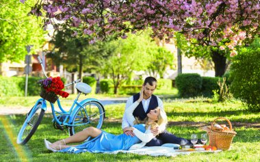 Mutluluğu hissetmek. Sakura çiçek ağacı altında romantik bir çift. Yeşil çimlerde birbirine aşık çiftler. Birlikte doğanın tadını çıkarıyoruz. Şehir parkında piknik yapıyoruz. Kadın ve erkek yemek sepetiyle rahatlar..