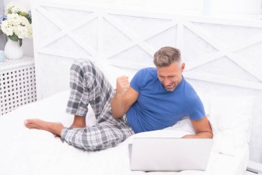 Evde başarılı bir serbest çalışan. Adam evde, yatakta serbest çalışıyor. Adam evde, yatak odasında serbest çalışıyor. Evde dizüstü bilgisayarlı bir adamın fotoğrafı..