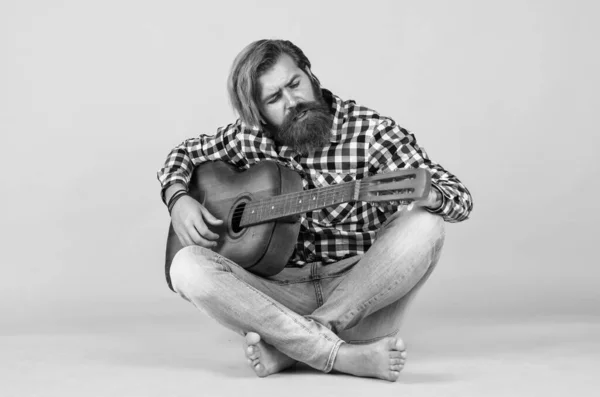 favorite tune. Portrait of happy bearded male playing guitar. a lonely musician. cheerful handsome mature man playing guitar and smiling while sitting on yellow background.