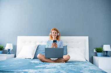 Neşeli kadın internette alışveriş yapıyor. Kadının evde telefonla alışverişi var. İnternetten kulaklıklı kadın alışverişi.