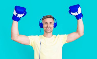 Stüdyoda boks eldivenli mutlu adam boksörü. Spor eldivenli bir boksör kulaklık takıyor. Boks eldiveni giymiş boksör adamın fotoğrafı. Boks eldivenli adam mavi üzerine izole edilmiş..