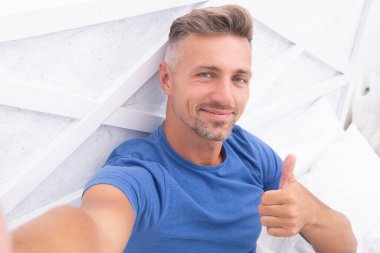 Telefon gömlekli selfie adam, başparmağını kaldır. Yatakta telefonlu selfie çeken adam. Evde telefonlu selfie çeken adamın fotoğrafı. Yatak odasında telefonlu selfie çeken adam..