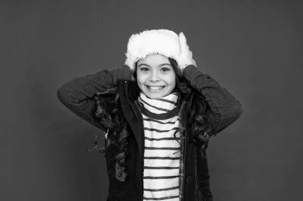 express positive emotion. winter fashion. positive kid with curly hair in earflap hat. teen girl on red background. portrait of child wearing warm clothes.
