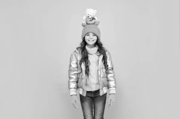 happy kid in puffer jacket and hat. childhood. teen girl hold toy bear. child wear warm clothes on blue background. express positive emotion. winter fashion. love toy for valentines day.
