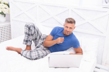 Evde, yatak odasında serbest çalışan neşeli bir adam. Evde dizüstü bilgisayarlı serbest çalışan bir adamın fotoğrafı. Evde serbest çalışan bir adam var. Adam evde, yatakta serbest çalışıyor..