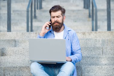 Kafası karışık adamın dışarıda online video iletişimi var. Adamın dışarıda çevrimiçi video bağlantısı var. Adamın merdivenlerde online video bağlantısı var. Adamın dizüstü bilgisayarında video bağlantısı var..