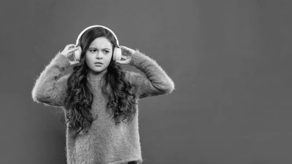 serious kid wear sweater. express emotion. autumn fashion. teen girl in earphones. modern life in childhood. listening audio book. copy space. child listen music in headphones.