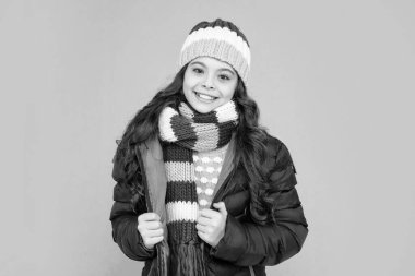 happy kid with curly hair in hat and scarf. teen girl in puffer jacket on blue background. portrait of child wearing warm clothes. express positive emotion. winter fashion.