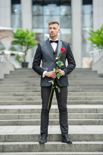 special occasion formalwear. full length of elegant man with rose for special occasion. tuxedo man outdoor at special occasion.