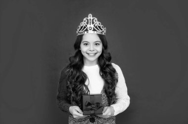 happy child in queen crown. princess in tiara hold box. kid with present. teen girl wear diadem on red background.