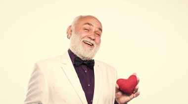 Gerçek bir beyefendi. Yakışıklı sakallı adam smokin giyer. Yaşlı centilmen romantik ruh. Adam sevginin kalp sembolünü taşıyor. Romantizm ve flört. Yaşlılar için flört hizmetleri. Centilmen kavramı.