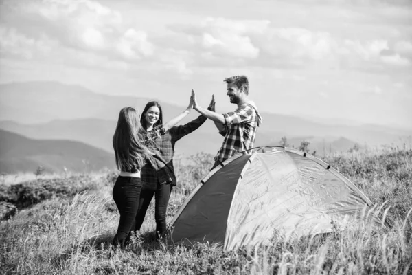 Well done. Camping gear. Camping tent. Good job. Teamwork concept. Hiking activity. Friends set up tent on top mountain. Camping equipment. Weekend in mountains. Man and girls having fun in nature.