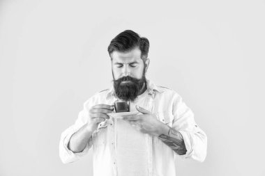 Serious caucasian man with closed eyes smelling tea holding cup and saucer yellow background, break.