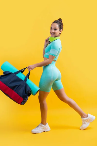happy fitness woman in sportswear walk with sport bag in studio. fitness woman in sportswear isolated on yellow background. fitness and sportswear.