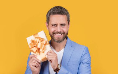 happy guy with gift box for holiday. photo of guy holding occasion gift box. guy hold gift box isolated on yellow background. guy hold gift box in studio.